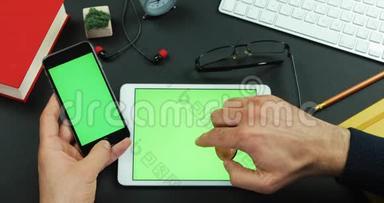 男人拿着绿色屏幕的智能手机，桌子上有绿色屏幕，右手拿着比特币